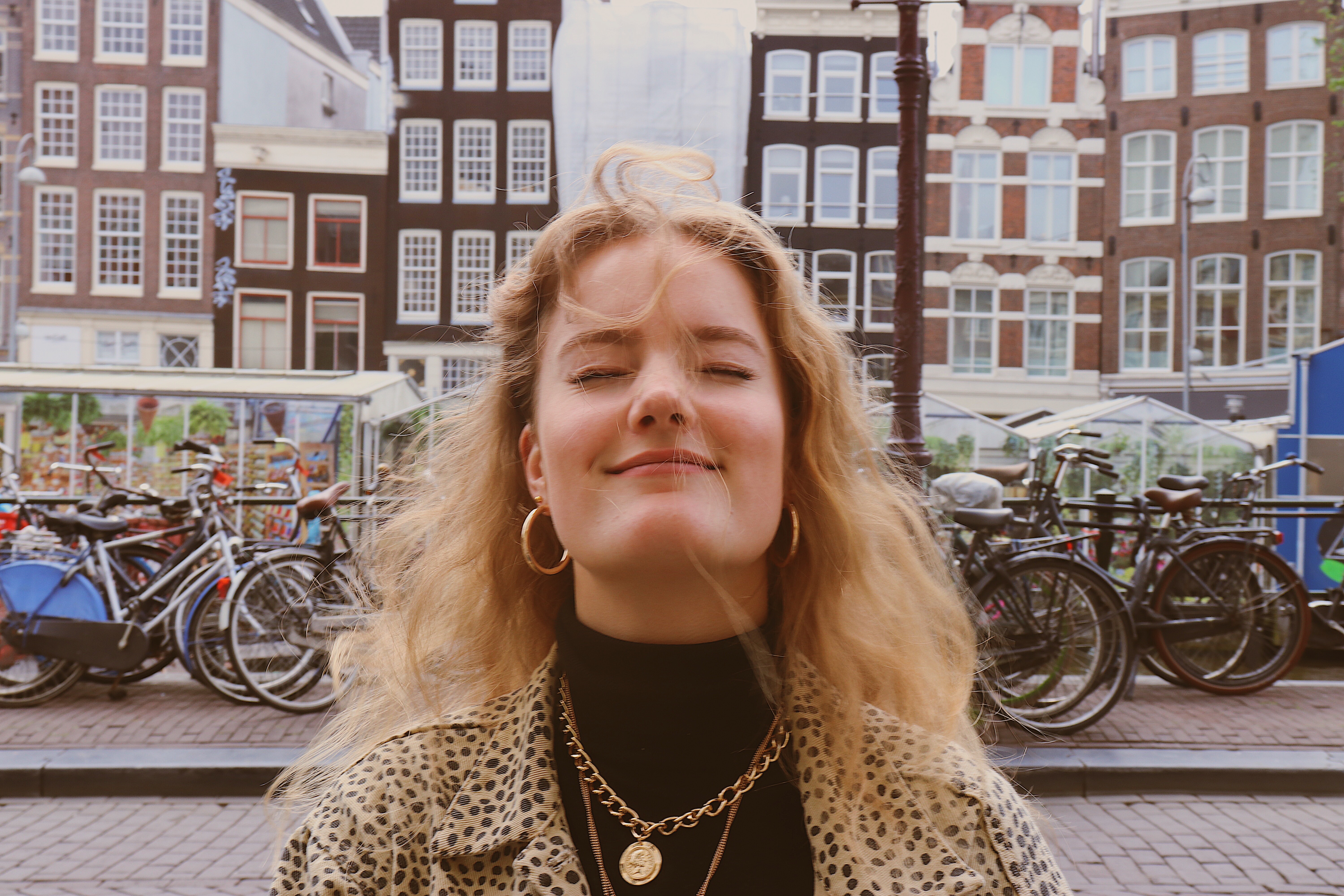 Photo of Mandy, Candace's friend from Amsterdam, Netherlands, with windswept hair, sitting at a cafe, in front of the canals with bikes behind her.