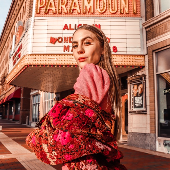 Candace in a pink puffy sleeve turtleneck body con dress from Forever 21 and brown and pink floral jacket from Urban Outfitters. She has straight hair and natural makeup. She stands in front of the Paramount Theater in Downtown Anderson.