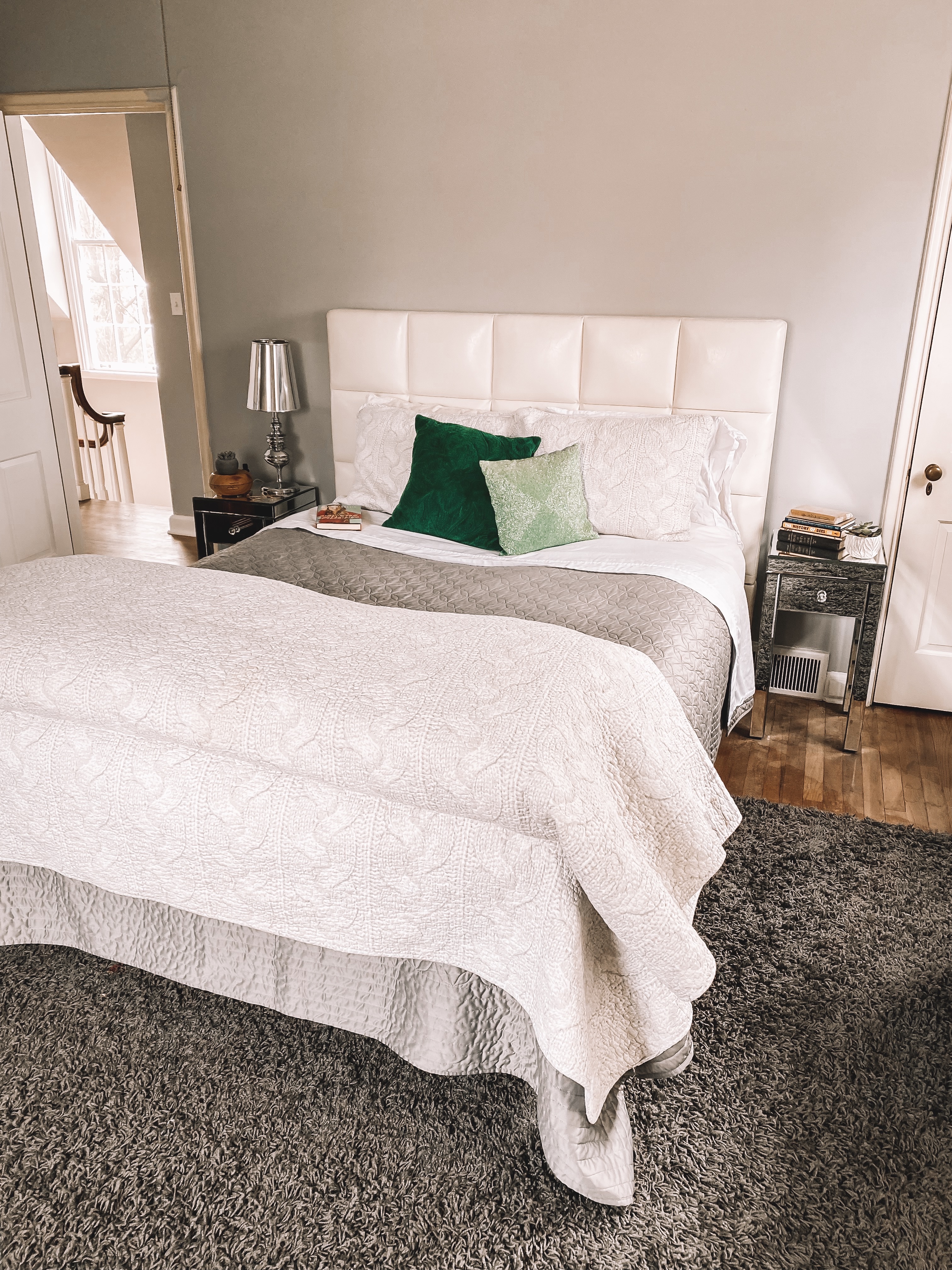 Photo of Candace's bedroom. She has white sheets, a grey comforter, a white quilted duvet, white pillows, and emerald green decorative pillows as well.