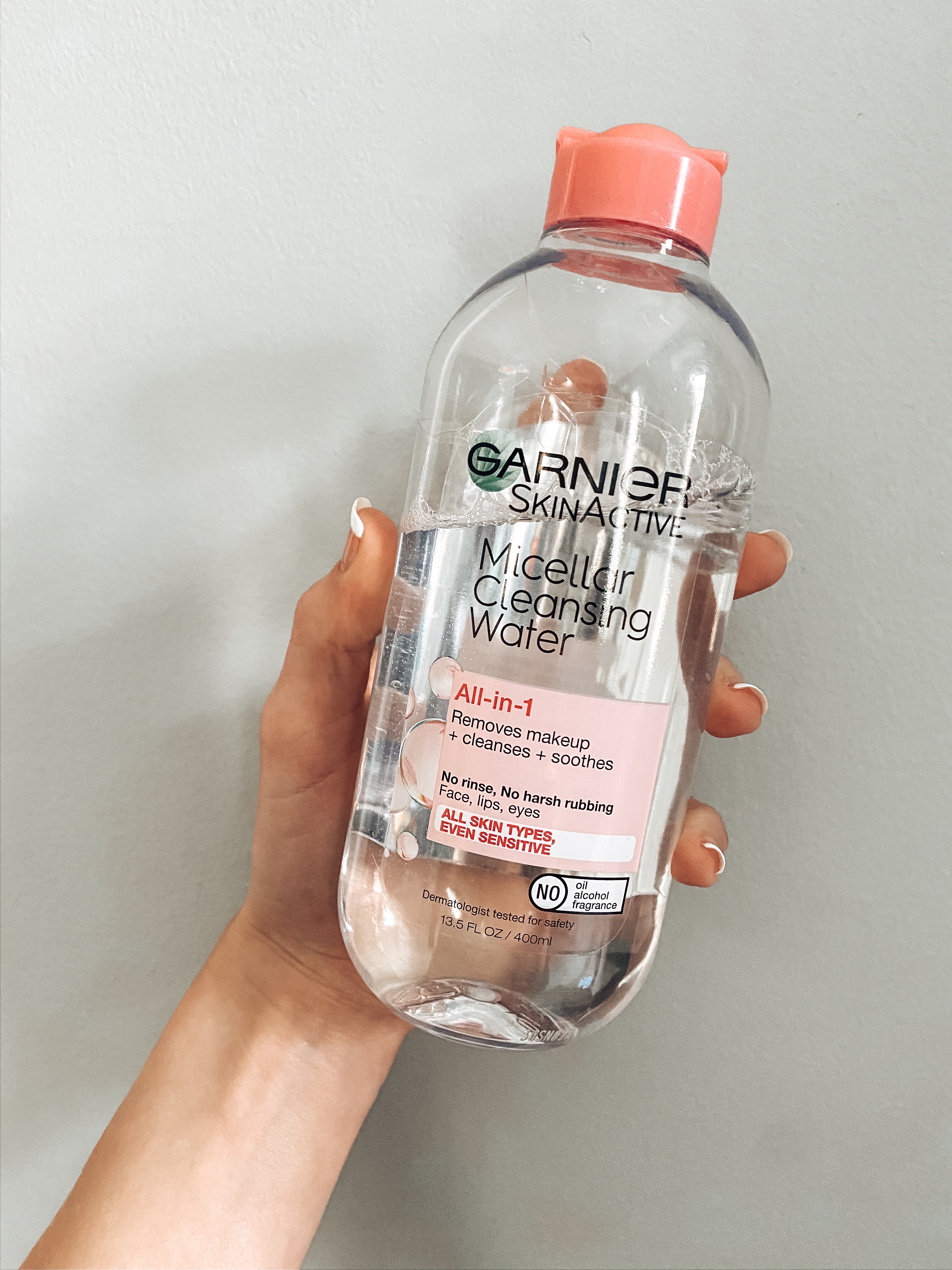 Candace's hand holind a bottle Garnier's Micellar Cleansing Water in front of a grey wall. 