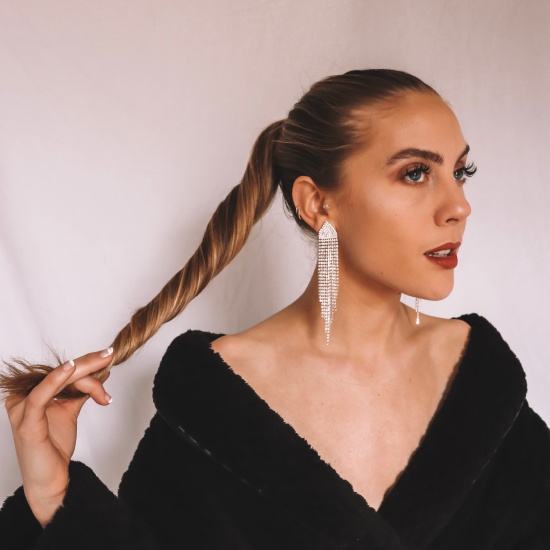 Photo of Candace in front of a white backdrop, she's wearing a black robe and diamond drop earrings with her hair in a pony tail and dramatic makeup.