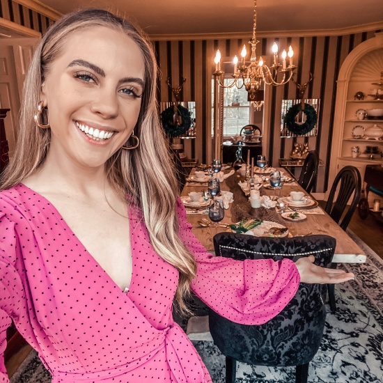 Candace smiling and wearing a pink polkadot dress from Nasty Gal in front of her Seder tablescape.
