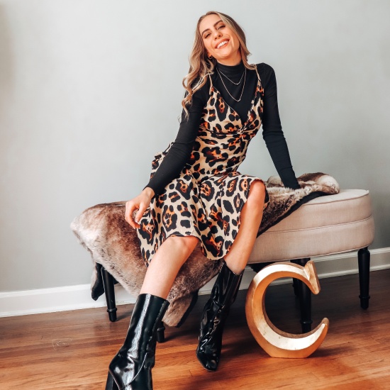 Candace sitting and smiling in a leopard dress from Nasty Gal, black turtleneck, and black shiny calf boots.